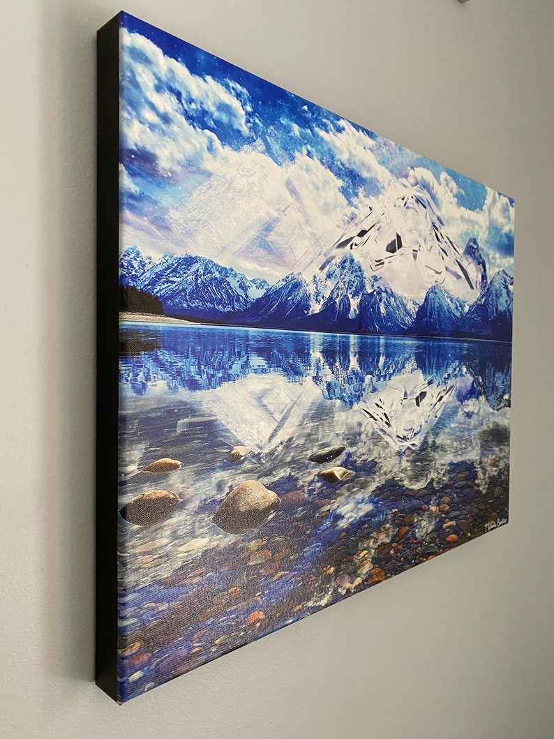 May include: A canvas print of a snowy mountain range reflected in a still lake. The sky is a vibrant blue with fluffy white clouds. The water is clear and blue, with rocks visible at the bottom.