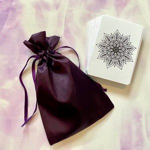 May include: A set of white cards with black mandala designs, packaged in a purple velvet drawstring bag.