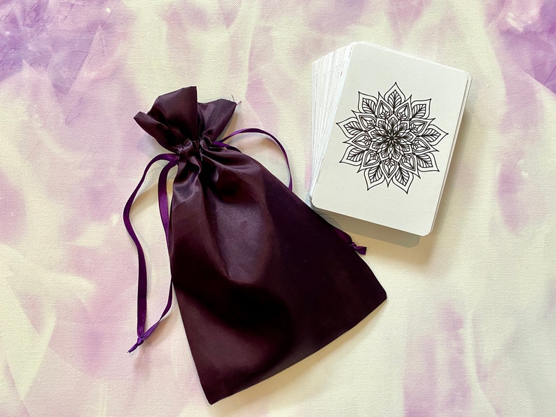 May include: A set of white cards with black mandala designs, packaged in a purple velvet drawstring bag.