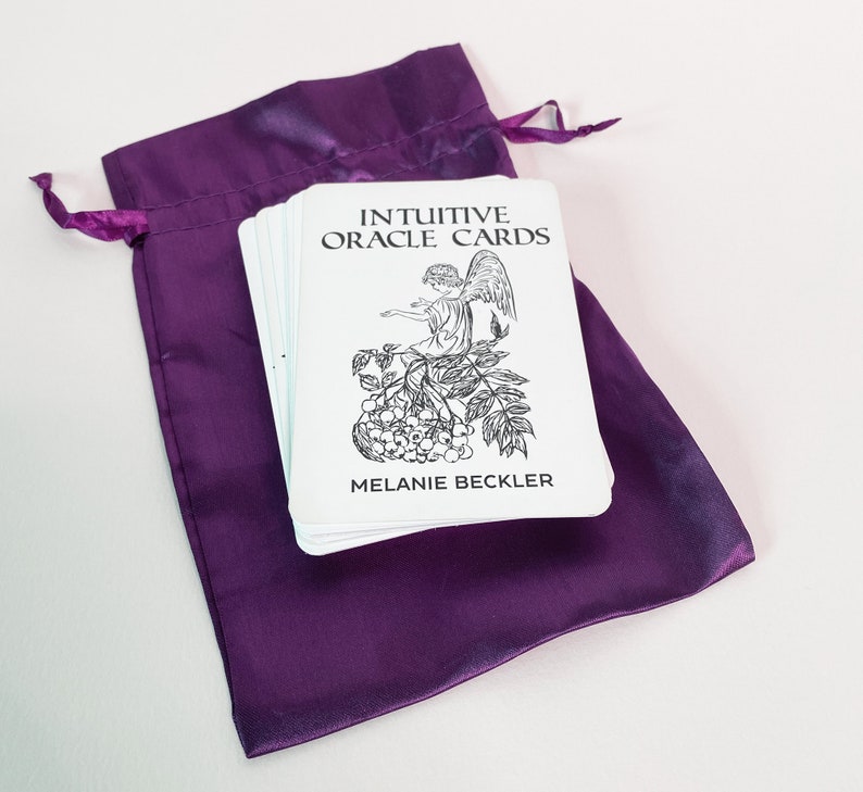May include: A purple velvet pouch containing a deck of Intuitive Oracle Cards by Melanie Beckler. The cards feature a black and white illustration of an angel sitting on a branch with berries.