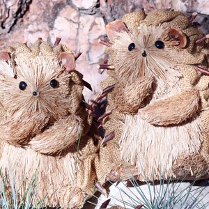 May include: Two brown and beige handmade hedgehog figurines with twig spines. The hedgehogs are made of burlap and have a brush-like texture.