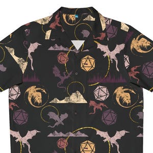 May include: Black button-up shirt with a repeating pattern of dragons, dice, and mountain silhouettes in shades of purple, gold, and beige. The short-sleeved shirt has a classic collar and is made of a lightweight fabric.