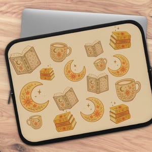May include: A beige laptop sleeve with a black border, featuring a repeating pattern of books, crescent moons, and coffee mugs in shades of brown and orange. The design has a whimsical, bohemian aesthetic.