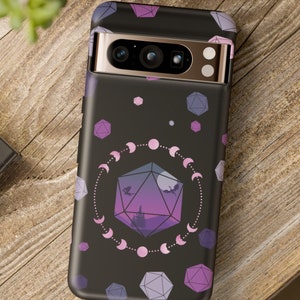 May include: A black phone case with a purple and pink design featuring a large, geometric die with a crescent moon pattern. The case has a camera cutout and a gold trim.