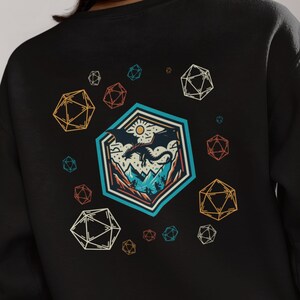 May include: Black sweatshirt with a graphic print of a mountain landscape with a flying dragon inside a large, colorful, geometric shape. The design is surrounded by smaller geometric shapes.
