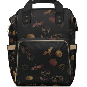 May include: Black backpack with a gold and bronze dragon and geometric dice pattern. Features a front pocket, side pockets, and a top handle. The bag has a neutral beige trim and gold zippers.
