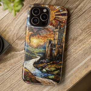 May include: A smartphone case featuring a stained-glass design with a castle, dragon, and river scene. The case has a colorful mosaic pattern with shades of orange, yellow, blue, and brown. The case is on a wooden surface.