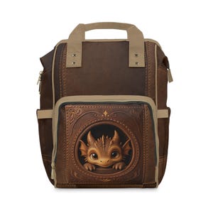 May include: A dark brown backpack featuring a tan top handle and trim. The front pocket displays a circular embossed frame containing a detailed illustration of a small, light brown dragon with large eyes and horns peering out from within.
