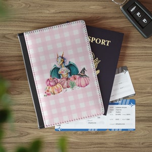 May include: Pink and white checkered passport holder with a dragon holding a teacup and surrounded by pumpkins. The text "SPORT" is visible on a blue passport.