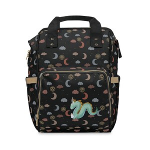 May include: Black backpack with a whimsical dragon design. The backpack has a gold zipper and a gold trim. The fabric has a repeating pattern of moons, clouds, and stars.
