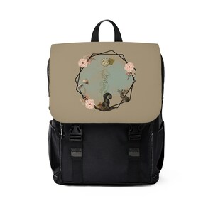 May include: A black backpack with a beige front panel featuring a geometric design with a floral wreath, a dice, a mushroom, a hat, and a squirrel.