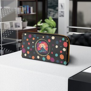 May include: Black leather wallet with a colourful geometric pattern and a mountain scene inside a circle. The wallet has a zip closure.