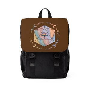 May include: A brown backpack with a black canvas base. The front flap features a watercolour illustration of a mushroom inside a multi-coloured, geometric shape surrounded by a circle of stars and crescent moons.