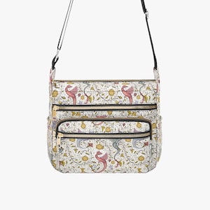 May include: White crossbody bag with a colorful floral and mythical creature pattern. The bag has three zippered compartments with gold-colored zippers and a black adjustable strap. The pattern includes pink seahorses, yellow flowers, and green foliage.