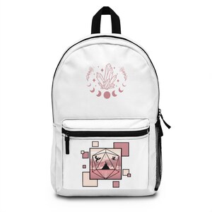 May include: White canvas backpack featuring a pink crystal and moon design on the front. The back pocket displays a pink and white geometric design with a silhouette of a mountain range and three flying dragons.