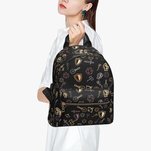 Mini PU leather backpack purse with fantasy RPG icons including dice, swords, shields, and spell symbols on a black background; front zipper pocket and top handle