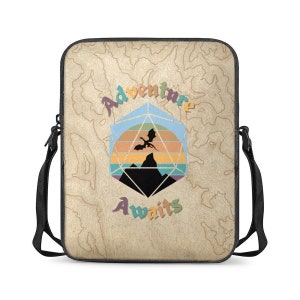 May include: A beige laptop sleeve with a black strap. The sleeve features a graphic of a 20-sided die with a dragon flying over a mountain range in a sunset. The text "Adventure Awaits" is written in a stylized font.