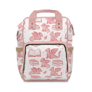 Può includere: Uno zaino bianco con un motivo di draghi e libri rosa. Lo zaino ha un manico, finiture e spallacci rosa. Il design include draghi rosa, libri e diamanti. Ha una tasca frontale e tasche laterali.