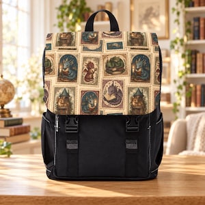 May include: A black backpack featuring a flap with a repeating pattern of rectangular postage stamp-style illustrations. The designs depict small dragons reading books, holding keys, and sleeping in various settings with candles and towers.