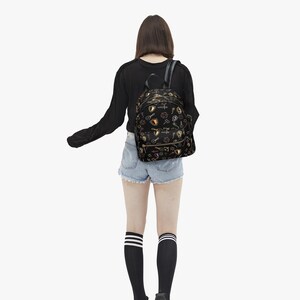 Mini PU leather backpack purse with fantasy RPG icons including dice, swords, shields, and spell symbols on a black background; front zipper pocket and top handle