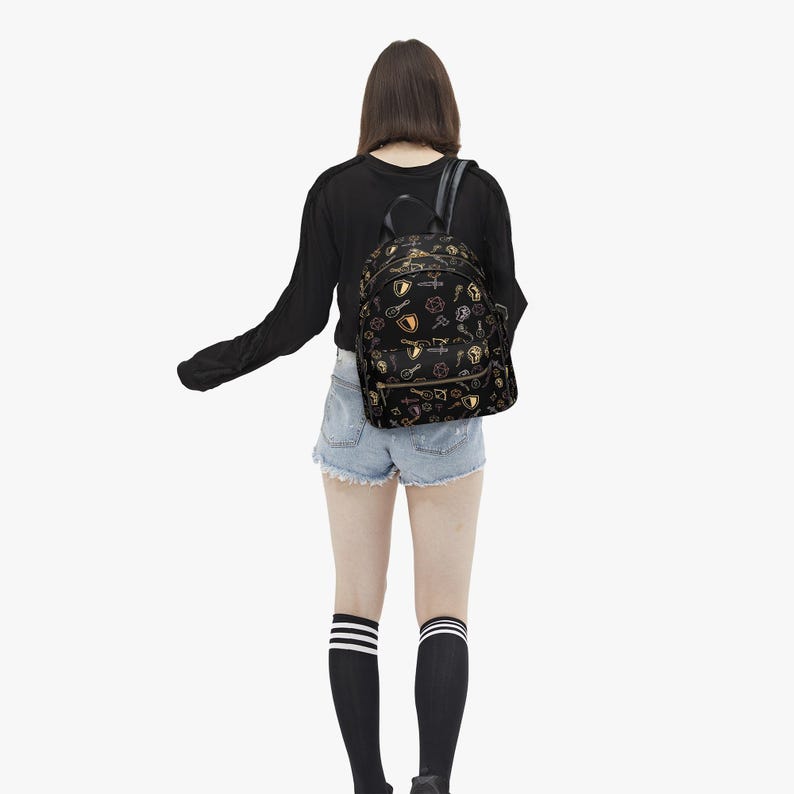 Mini PU leather backpack purse with fantasy RPG icons including dice, swords, shields, and spell symbols on a black background; front zipper pocket and top handle