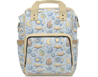 Puede incluir: Una mochila azul claro con un patrón caprichoso de dragones, libros, lunas y estrellas. La bolsa tiene un bolsillo frontal, bolsillos laterales y un asa superior. El ribete y el asa son de color beige.