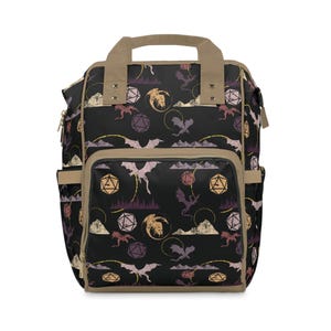 May include: Black backpack featuring a repeating pattern of dragons, dice, and mountain silhouettes in purple, gold, and tan. The bag has a tan handle and trim, with multiple pockets and a front flap.