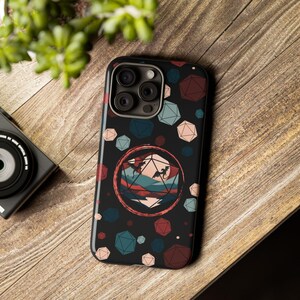 May include: A black phone case with a colorful design featuring a large red, white, and blue dice with a mountain landscape inside. The dice is surrounded by smaller dice in various colors.