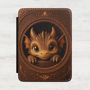 May include: A rectangular e-reader case featuring a brown, textured leather-like finish with an embossed circular frame. Inside the frame, a golden-brown dragon with large eyes and small horns peers out. The cover includes decorative gold scrollwork.