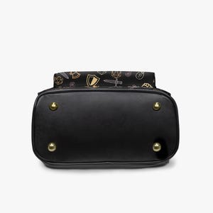 Mini PU leather backpack purse with fantasy RPG icons including dice, swords, shields, and spell symbols on a black background; front zipper pocket and top handle