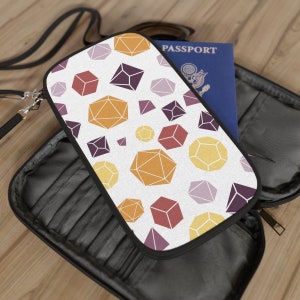 Könnte beinhalten: Ein schwarzer Reisepass-Etui mit Reißverschluss und einem weißen Stoffeinsatz mit einem geometrischen Muster aus bunten Würfeln. Der Stoffeinsatz hat einen weißen Hintergrund mit einem sich wiederholenden Muster aus orangefarbenen, gelben, roten, violetten und grauen Würfeln.