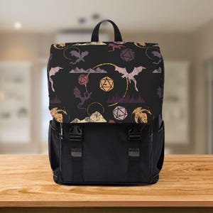 May include: Black backpack with a flap featuring a repeating pattern of dragons, dice, and mountain silhouettes in gold, purple, and orange. The backpack has a black body with two front straps and a top handle.
