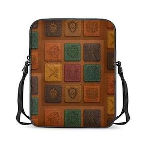May include: A brown crossbody bag with a repeating pattern of square patches. Each patch features a different fantasy-themed icon, such as a dragon, shield, or treasure chest. The bag has a black strap and a rectangular shape.