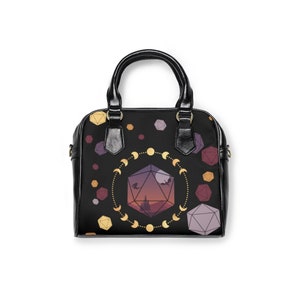May include: Black leather handbag with a geometric design featuring a large, multi-colored dice with a sunset scene inside. The dice is surrounded by a circle of gold crescent moons.