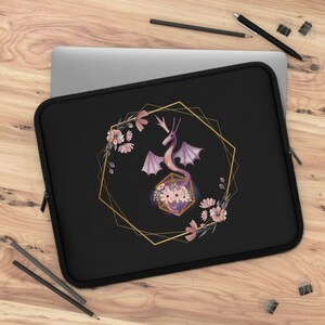 May include: A black laptop sleeve with a gold geometric frame and a purple dragon inside a pink flower. The dragon is surrounded by pink flowers.