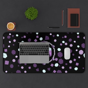 Könnte beinhalten: Eine schwarze Schreibtischunterlage mit einem sich wiederholenden Muster aus violetten, rosa und weißen geometrischen Formen. Ein Laptop, eine Maus und eine Tasse Kaffee befinden sich auf der Unterlage.