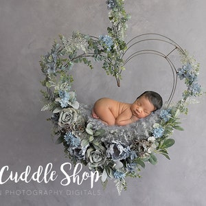 Könnte beinhalten: Ein Neugeborenes schläft in einem grauen und blauen, herzförmigen Blumenkranz. Der Kranz besteht aus künstlichen Blumen und Grünpflanzen. Der Text "Tiny Cuddle Shop" steht unter dem Kranz.