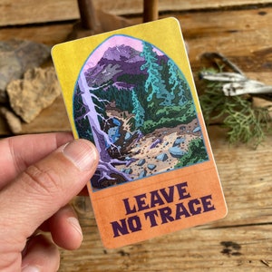 May include: A sticker with a colorful illustration of a mountain scene and the text "LEAVE NO TRACE" in a purple font on an orange background.