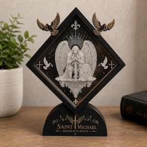 Può includere: Una cornice nera a forma di rombo con l'illustrazione di un angelo con una spada e un leone. Due uccelli color oro sono fissati agli angoli superiori. La base è nera con il testo dorato SAINT MICHAEL DEFEND US IN BATTLE.