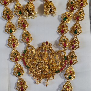 May include: A gold-tone necklace set with two strands of intricate, ornate designs featuring red and green gemstones. The set includes a pair of matching earrings with a similar design.