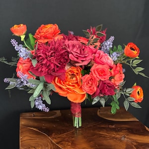 Könnte beinhalten: Ein lebendiger Strauß mit roten, orangefarbenen und violetten Blumen. Der Strauß enthält Rosen, Pfingstrosen und Lavendel.