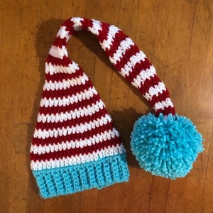 May include: A red and white striped crocheted hat with a blue pom-pom on top.