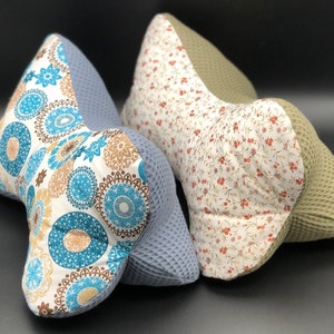 Könnte beinhalten: Zwei dekorative Kissen mit unterschiedlichen Mustern. Ein Kissen hat ein blaues und braunes geometrisches Muster, das andere hat einen weißen Hintergrund mit kleinen roten Blumen. Beide Kissen sind aus einem weichen, strukturierten Stoff gefertigt.