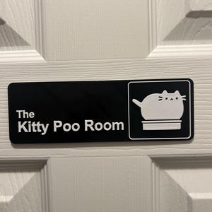 Op de afbeelding: Een zwart-wit bord met de tekst "The Kitty Poo Room" en een cartoonkat in een kattenbak.