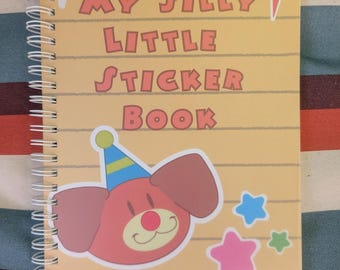 May include: A spiral-bound notebook with a yellow cover featuring horizontal lines and the text "MY SILLY LITTLE STICKER BOOK" in red. The cover displays a red cartoon dog wearing a blue party hat, two yellow diamond shapes, a red lightning bolt, and three small stars in blue, pink, and green.