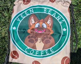 May include: A beige drawstring bag with a green and white circular logo that reads "YEEN BEANS COFFEE." The logo features a cartoon fox character. Brown coffee beans are scattered across the bag's surface. Black drawstrings are visible.