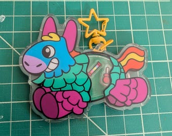 May include: A clear acrylic keychain featuring a colorful piñata character with a blue head, green body, and pink accents. The design includes a yellow star-shaped clasp and a small internal compartment containing tiny loose candy-shaped charms.