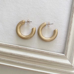 May include: A pair of gold hoop earrings. The earrings are simple and elegant, with a smooth, rounded shape.