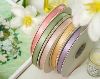 May include: A spool of six different colored satin ribbon. The colors are pink, green, light pink, peach, purple, and white. The ribbon is wound around a white cardboard spool.