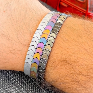 May include: A bracelet made of three rows of iridescent metal chevron beads. The beads are in shades of silver, gray, purple, blue, yellow, and orange.